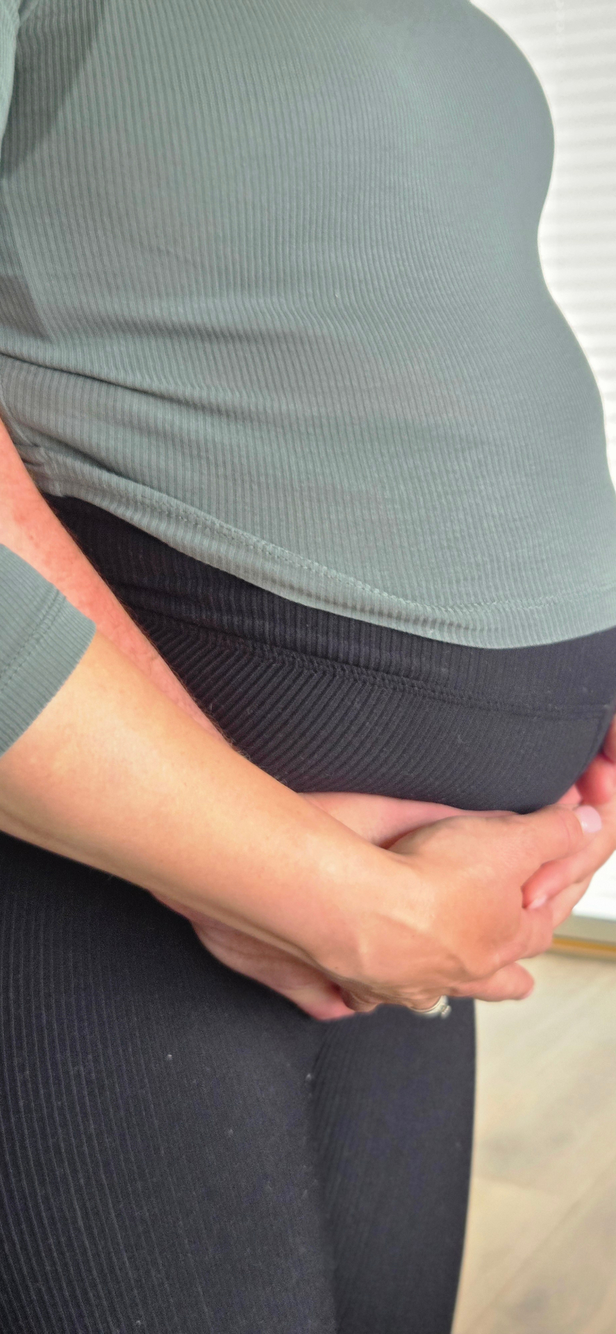 Gravid mage i grønt med en hånd under magen
